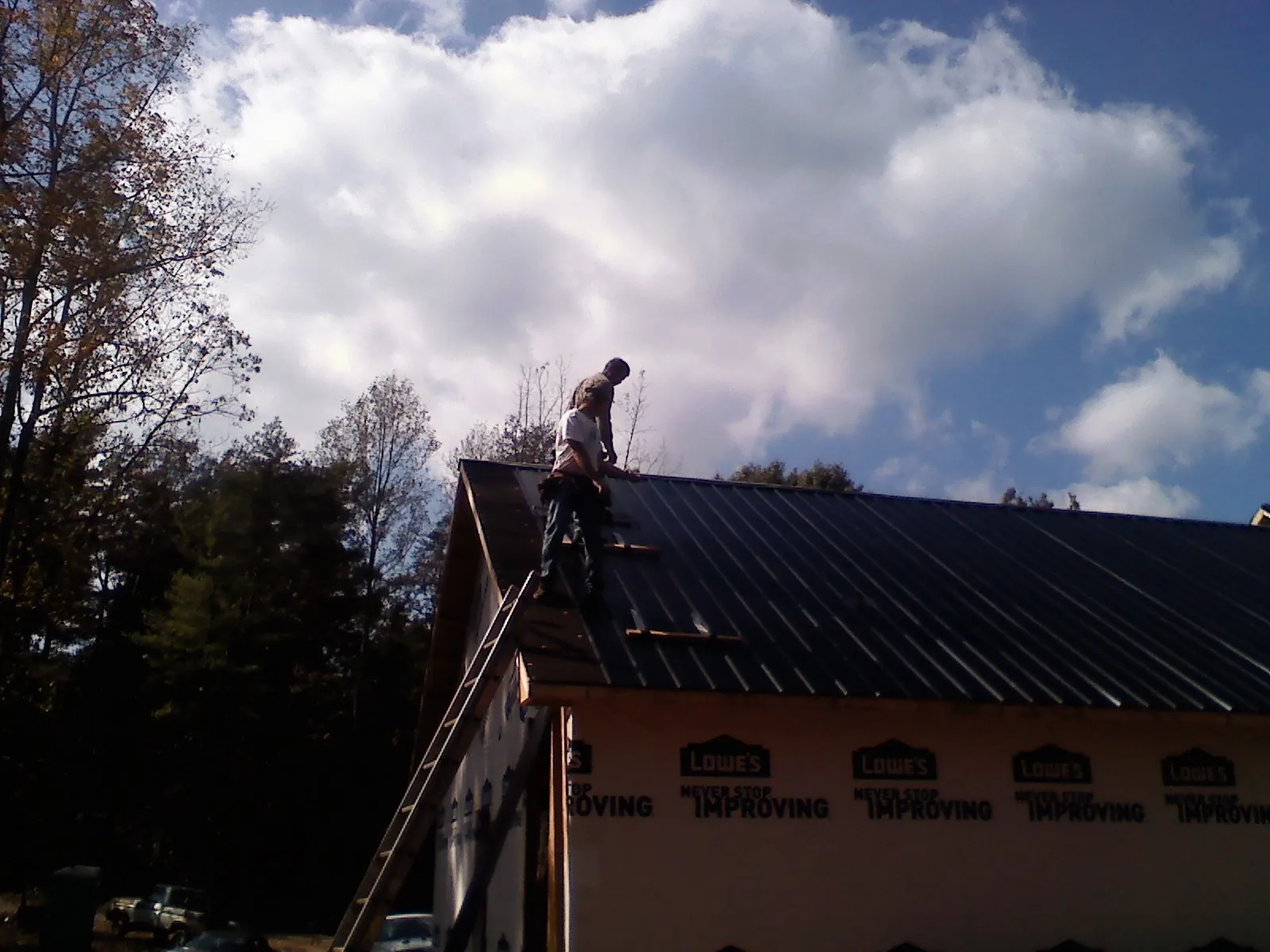 Roofer fastening dark metal panels high against a cloudy sky, from a Roof Inspection job in Gardiner